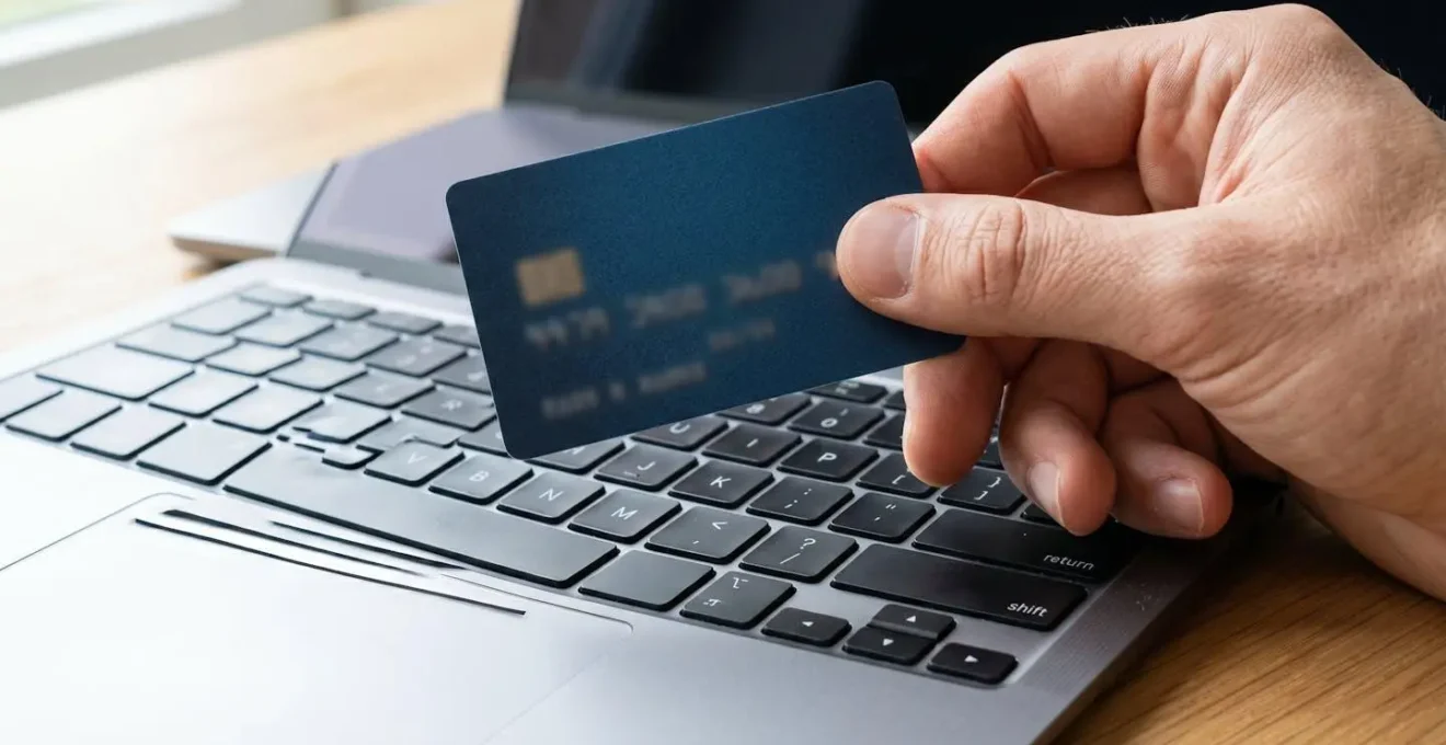 Gros plan d'une main tenant une carte bancaire moderne au-dessus d'un clavier d'ordinateur portable